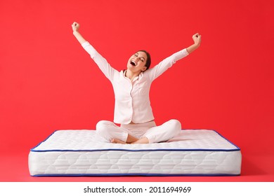 Happy young woman sitting on mattress against color background