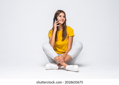 Happy Young Woman Sitting On The Floor Talking On A Mobile Phone On White Background