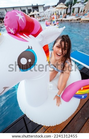 Happy young woman sitting on inflatable unicorn toy mattress