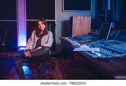 Happy Young Woman Sitting In Sound Recording Studio. Female Music Composer Sitting By Sound Mixing Console.