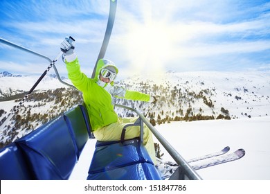Happy young woman skier sitting on ski lift chair, smiling and happily lifting her hands