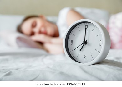 Happy Young Woman Sleeping Near Bed Side Alarm Clock. Calm Healthy Morning Sleep Of Woman In Pajamas. Morning Routine And Wake Up From Alarm Clock