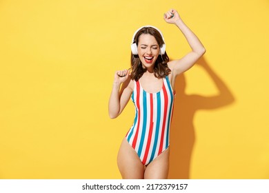 Happy young woman slim body wear red blue swimsuit listen music in headphones dance sing song have fun isolated on vivid yellow color wall background studio. Summer hotel pool sea rest sun tan concept