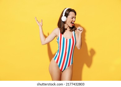 Happy young woman slim body wear red blue swimsuit listen music in headphones dance sing song have fun isolated on vivid yellow color wall background studio. Summer hotel pool sea rest sun tan concept