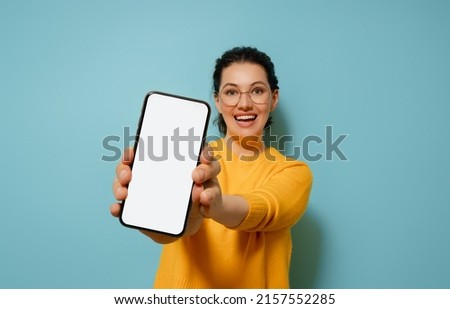 Happy young woman with smartphone on background of blue wall. Blank screen mobile phone for graphic montage.