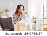 Happy young woman smelling clean laundry with pleausure, fresh smell in house after washing. Housewife, female cleaner with basket textile enjoy clothes aroma, fragrance, nice scent, using conditioner