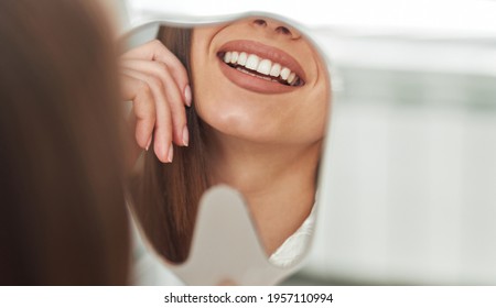 Happy Young Woman Smiling Checking Out Her Perfect Healthy Teeth In The Mirror Close Up, At The Dentist Office