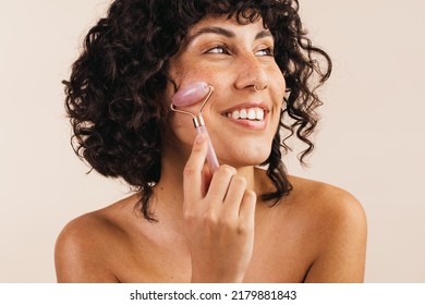 Happy Young Woman Smiling Cheerfully While Massaging Her Face With A Jade Roller. Body Conscious Young Woman Taking Care Of Her Skin Using A Cosmetic Beauty Stone.