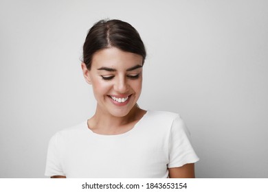 Happy young woman smiling wearing white T-shirt looking down. Space for text.