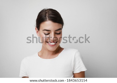 Happy young woman smiling wearing white T-shirt looking down. Space for text.