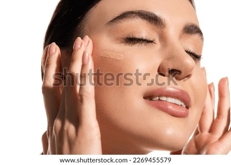 happy young woman with soft skin applying makeup foundation with fingers isolated on white