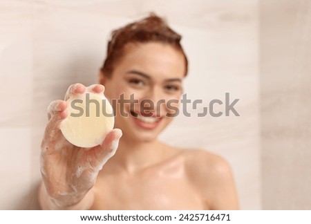 Happy young woman with solid shampoo bar in shower, selective focus. Space for text