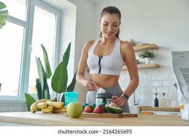 Happy Young Woman In Sports Clothing Preparing Protein Cocktail At Home