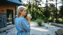 Happy Young Woman Standing In Garden Near Cottege And Enjoying Cup Of Morning Coffee On Summer Vacation In Mountains.