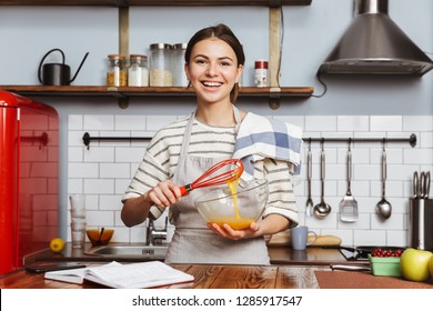 Happy young woman standing at the kitchen at home, mixing eggs in a bowl - Powered by Shutterstock