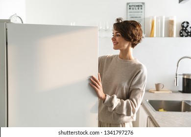 Happy young woman standing at the opened fridge