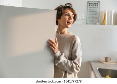 Happy young woman standing at the opened fridge