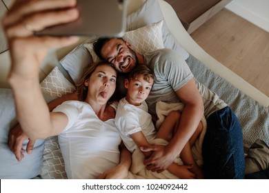 Happy young woman sticking out her tongue and taking selfie with her crazy family. Family lying on bed with funny facial expression and taking selfie at home. - Powered by Shutterstock