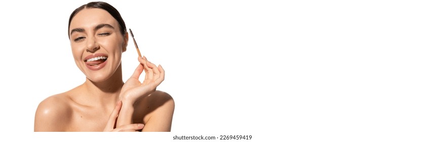 jovencita feliz sacando la lengua mientras sostiene el cepillo de cejas aislado en blanco, pancarta