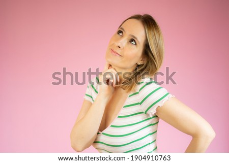 Happy young woman in striped t-shirt thinking over pink background.