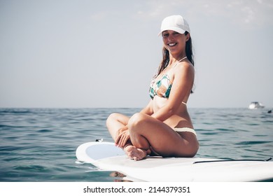 Happy young woman in swimsuit doing yoga on sup board in calm sea, early morning. Balanced pose - concept of healthy life and natural balance between body and mental development