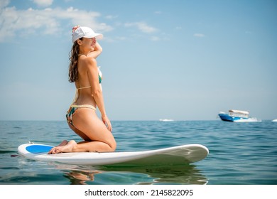 Happy young woman in swimsuit doing yoga on sup board in calm sea, early morning. Balanced pose - concept of healthy life and natural balance between body and mental development