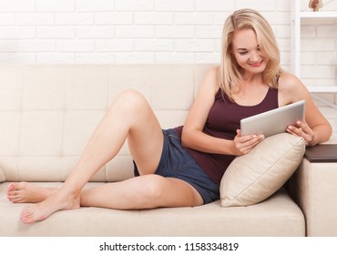 Happy young woman with tablet pc laying on sofa. Training concept and work remotely