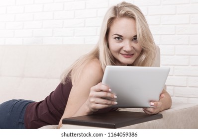 Happy young woman with tablet pc laying on sofa. Training concept and work remotely