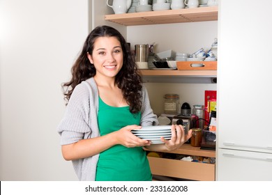 Happy Young Woman Taking Out Dishware Of The Cupboard To Set The Table