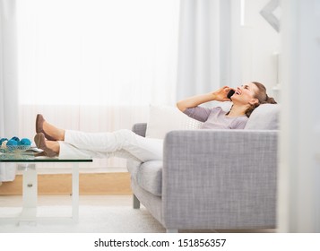 Happy Young Woman Talking Cell Phone While Sitting On Sofa