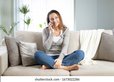 Happy Young Woman Talking On The Phone At Home, Smiling Female Holding Smart Phone And Making Call In Living Room