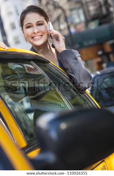 A happy young\
woman talking on her mobile cell phone by a yellow taxi cab. Shot\
on location in New York City