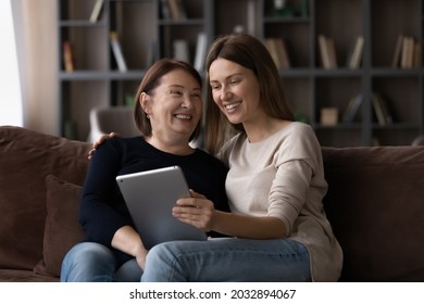 Happy young woman teaching older senior retired mother using digital computer tablet applications, sitting together on sofa. Joyful multigenerational female family using modern tech gadget at home. - Powered by Shutterstock