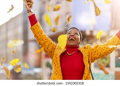 Happy young woman throwing dry leaves in urban area
 - Shutterstock ID 1592305318