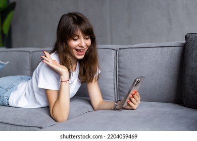 Happy Young Woman With Toothy Smile Waving Hand, Looking At Camera, Sitting On Couch At Home, Vlogger Recording Webinar, Using Webcam, Chatting Online, Making Video Call, Remote Job Interview