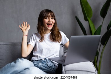 Happy Young Woman With Toothy Smile Waving Hand, Looking At Camera, Sitting On Couch At Home, Vlogger Recording Webinar, Using Webcam, Chatting Online, Making Video Call, Remote Job Interview