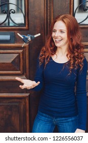 Happy Young Woman Tossing The Keys To Her Home In The Air As She Stands In Front Of Large Double Entrance Doors With A Beaming Smile