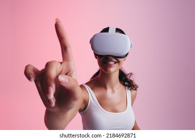 Happy young woman touching virtual space with her finger in a studio. Young woman smiling cheerfully while wearing a virtual reality headset. Carefree young woman exploring 3D technology.