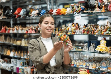Happy young woman tourist buys traditional spanish souvenirs - mosaic bull figurines