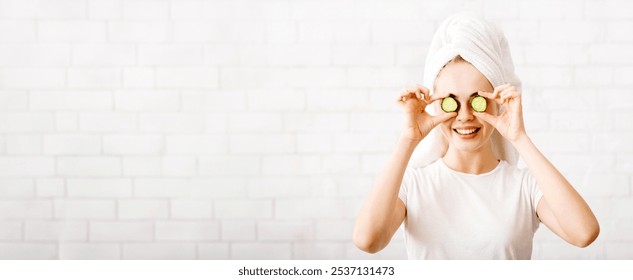 Happy young woman with towel on head covering eye with cucumber slices, face care - Powered by Shutterstock