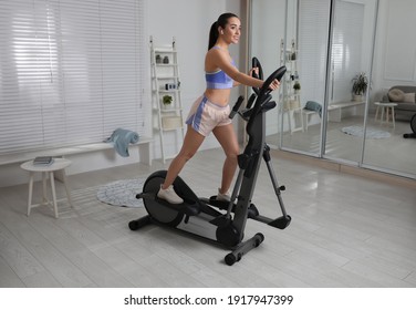 Happy young woman training on elliptical machine at home - Powered by Shutterstock