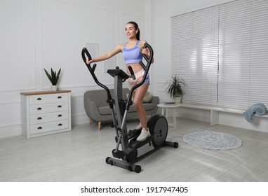 Happy Young Woman Training On Elliptical Machine At Home