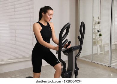 Happy Young Woman Training On Elliptical Machine At Home