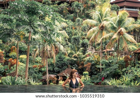 Happy young woman in a tropical infinity pool. Luxury resort on Bali island.