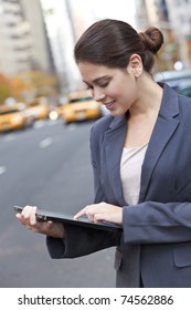 A Happy Young Woman Using Her Tablet Computer Outside In An American City With Yellow Taxis Behind Her. Shot On Location In New York City