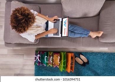 Happy Young Woman Using Laptop With Multi Colored Shopping Bags On Carpet