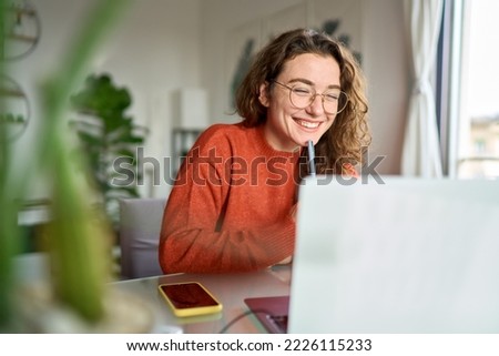 Happy young woman using laptop sitting at desk writing notes while watching webinar, studying online, looking at pc screen learning web classes or having virtual call meeting remote working from home.