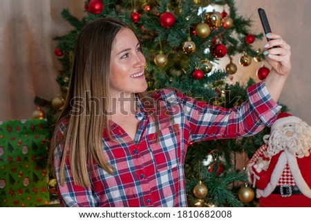 Happy young woman using smart phone to video phone call to greeting her family for Christmas in quarantine, with decoration and tree.