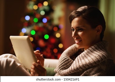 Happy young woman using tablet pc in front of christmas tree
