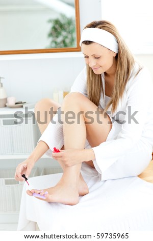 Happy young woman varnishing her toenails in the bathroom at home